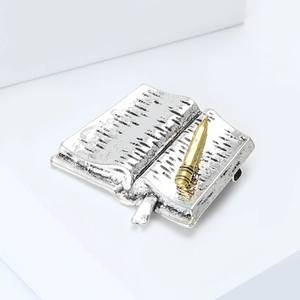 Detailed macro view of vintage open book brooch with silver texture and golden pencil detail