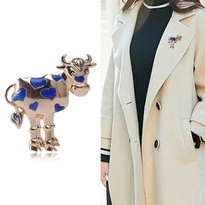 Golden cow brooch with blue heart enamel patterns shown on white and worn on a beige coat
