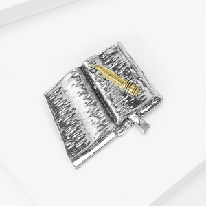 Macro detail of vintage book-shaped brooch with golden pen on a white background