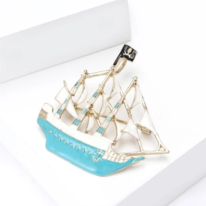 Macro view of sailboat brooch with white enamel sails and blue oil drip finish