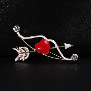 Dettaglio della spilla freccia di Cupido con cuore rosso e cristalli su sfondo nero