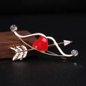 Dettaglio della spilla a freccia di Cupido con cuore rosso, smalto bianco e strass lucidi