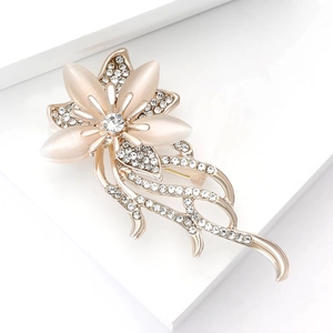 Elegant gold flower brooch with cat eye stone petals and rhinestones on a white base