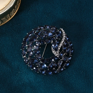 Detail of blue crystal wreath brooch with silver diamond accents on green velvet background