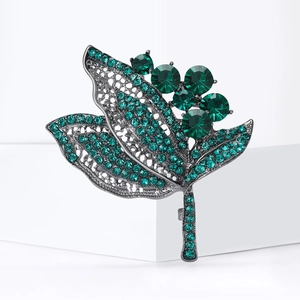 Broche élégante en forme de feuille verte avec cristaux sur fond blanc géométrique