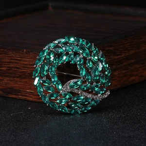 Detailed view of a green crystal wreath brooch with silver metal base and pin closure