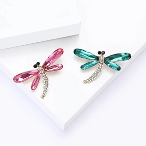 Elegant dragonfly brooches with vibrant pink and green crystals on minimalist display