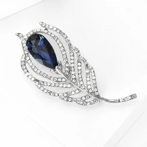 Detailed close-up of a silver feather brooch with white crystals and a large blue teardrop stone