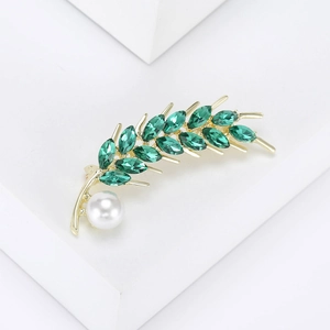 Détail de la broche épi dorée avec cristaux verts et une perle ronde blanche