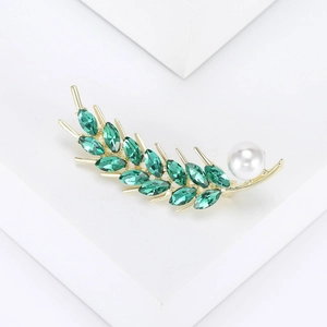 Macro detail of a wheat stalk brooch with green marquise crystals and a white pearl