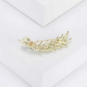 Élégante broche plume dorée avec perles et cristaux sur fond de pierre blanche épuré