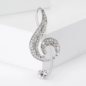 Macro detail of a silver musical note brooch featuring sparkling rhinestones and a large crystal