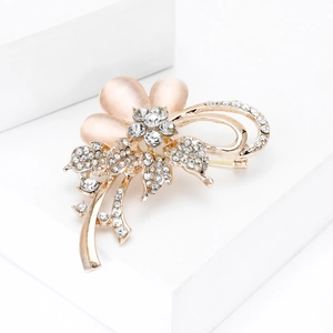 Broche fleur dorée élégante avec pierres œil de chat et strass sur socle blanc épuré