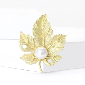 Élégante broche feuille d'érable dorée mate avec perle ronde sur socle blanc