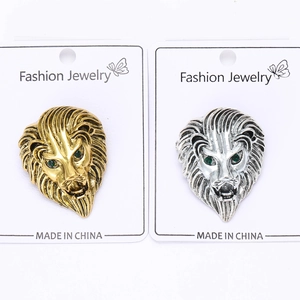 Detailed macro view of lion head brooches in gold and silver with green gemstone eyes