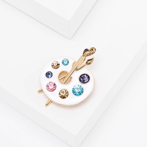 Detailed close-up of a white enamel artist palette brooch with colorful crystals and brushes
