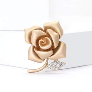 Matte gold rose brooch with sparkling crystal leaf on a white geometric display stand