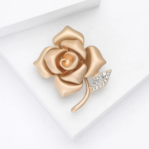 Elegant matte gold rose brooch with sparkling crystal leaf on a white geometric stage