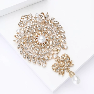 Elegant gold bow brooch with sparkling rhinestones and teardrop pearl on white blocks