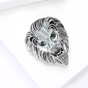 Vintage silver lion head brooch with green gem eyes on white display pedestal