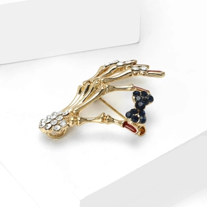 Detail view of gothic skeleton hand brooch with blue gemstone bow and red enamel on white background