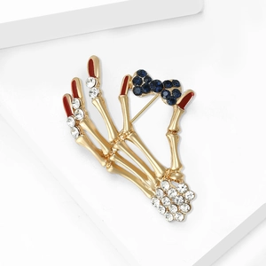 Macro shot of skull hand brooch with blue crystal bow and red enamel fingernails
