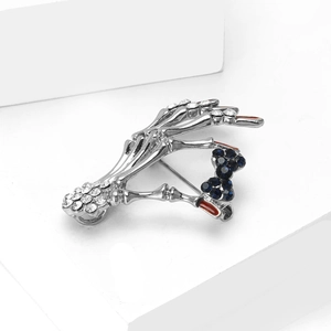 Detail of skull hand brooch with blue gemstone bow and rhinestones on a white stand