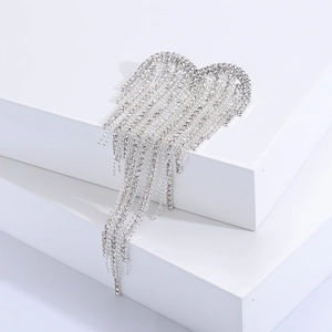 Détail de la broche cœur argentée avec glands en strass sur un podium blanc pur