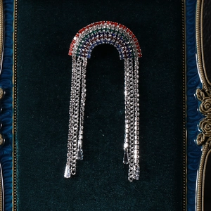 Detailed close-up of rainbow crystal brooch with silver tassel chains on velvet