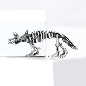 Spilla scheletro di dinosauro in argento vintage con occhio di strass verde su sfondo bianco