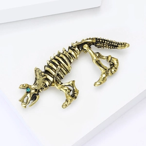 Vintage gold alloy dinosaur skeleton brooch with green gemstone eye on white background
