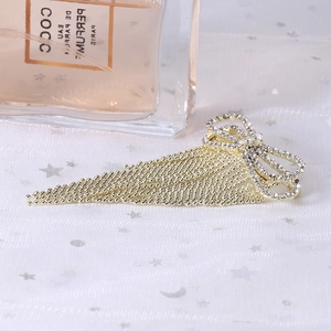 Close-up of elegant gold bow brooch with rhinestone inlay and beaded chain tassels