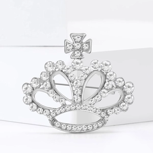 Élégante broche couronne en argent avec design en croix et strass blancs sur un bloc décor