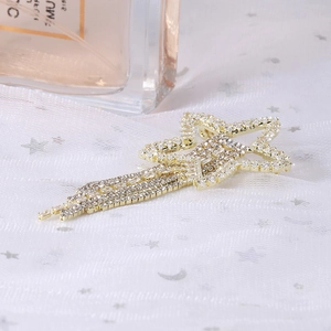 Detail of gold star brooch with shimmering rhinestone tassels on white mesh