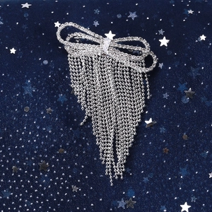 Close-up of elegant silver bow brooch with rhinestone tassels on starry velvet background