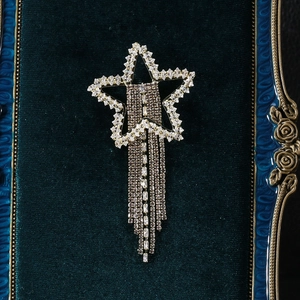 Close-up of sparkling star brooch with long tassels and rhinestones on green velvet