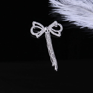 Dettaglio spilla a fiocco argento con nappe e strass su elegante sfondo nero specchiato