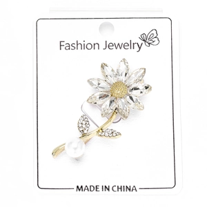 Detail shot of a crystal sunflower brooch with pearl drop on a white display card