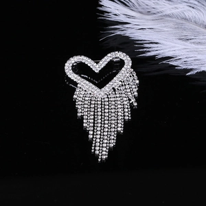 Détail d'une broche cœur argentée avec pampilles en strass sur fond de miroir noir
