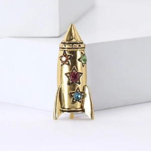 Vintage golden alloy rocket brooch with colorful star-shaped rhinestones on white block