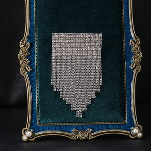 Detailed view of rhinestone fringe brooch displayed on vintage green velvet background