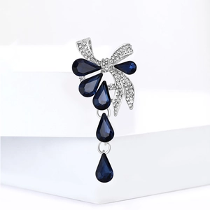 Broche nœud élégante avec gouttes de cristal bleu et strass scintillants sur métal argenté