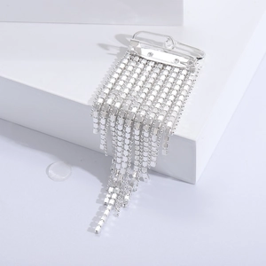 Macro detail of luxury silver tassel brooch with sparkling rhinestones on white geometric base