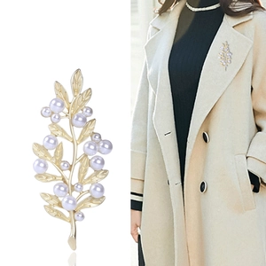 Elegant gold leaf brooch with white pearls shown on white background and on coat lapel