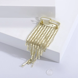 Detail view of a luxury gold tassel brooch with sparkling rhinestones on a white podium