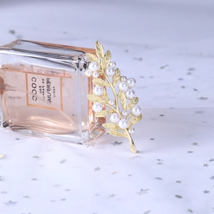 Detailed view of elegant golden leaf brooch with pearls resting against a perfume bottle