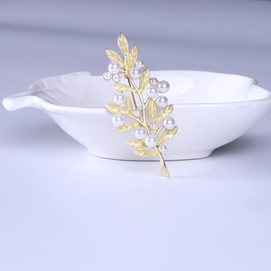 Close-up of golden leaf brooch with white pearls displayed on a white ceramic dish