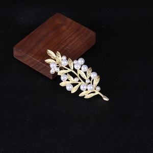Macro shot of gold leaf brooch with white faux pearls on a dark textured background