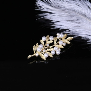 Detail of a matte gold leaf brooch with white pearls against a black reflective surface