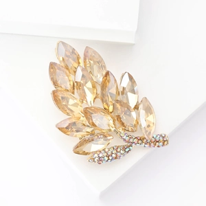 Detailed macro view of an amber gold leaf brooch with crystals on a white pedestal